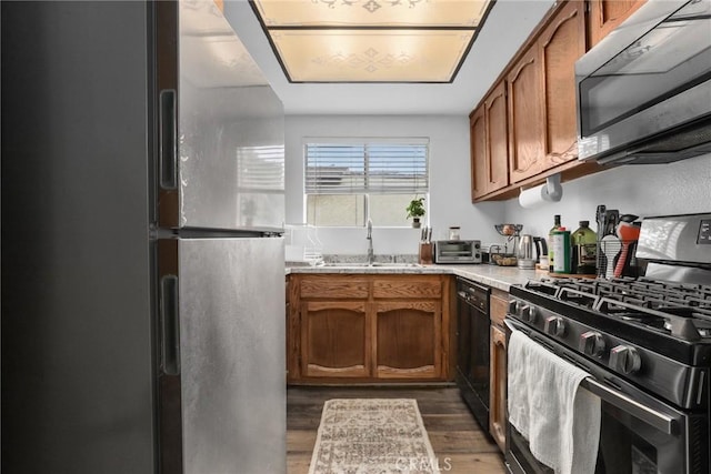 kitchen with brown cabinetry, dark wood-style flooring, appliances with stainless steel finishes, and a sink