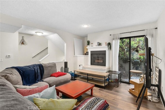 living room featuring wood finished floors, a textured ceiling, a fireplace with raised hearth, and recessed lighting