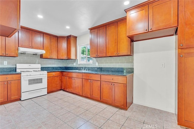 kitchen with under cabinet range hood, backsplash, light tile patterned flooring, brown cabinetry, and white gas range oven