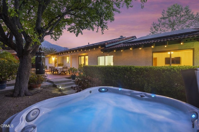 back of house featuring stucco siding, outdoor dining area, and a hot tub