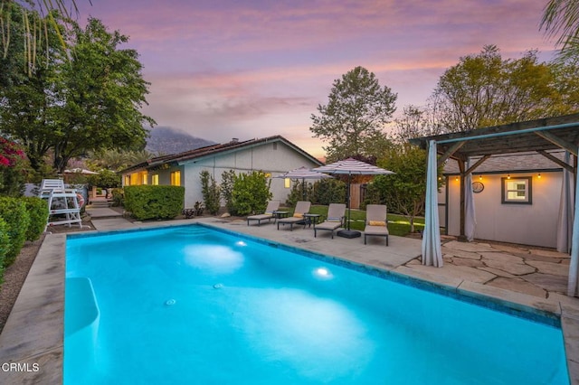 pool at dusk featuring an outdoor pool and a patio area