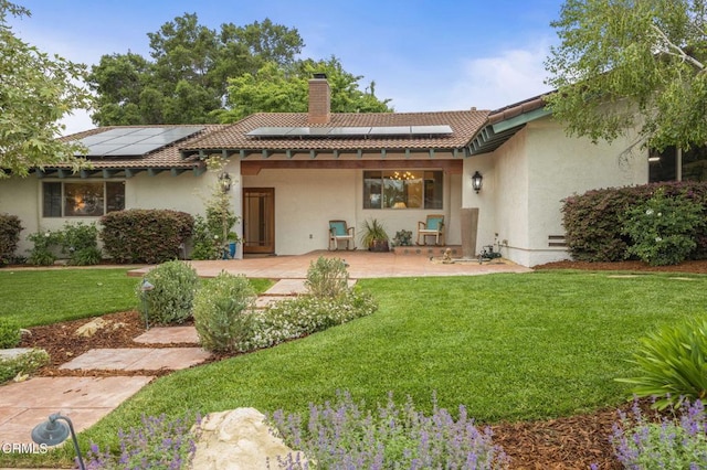 rear view of house featuring a patio, a chimney, roof mounted solar panels, and a yard