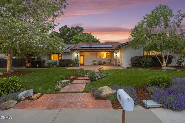 view of front facade featuring a front lawn, a chimney, solar panels, stucco siding, and fence
