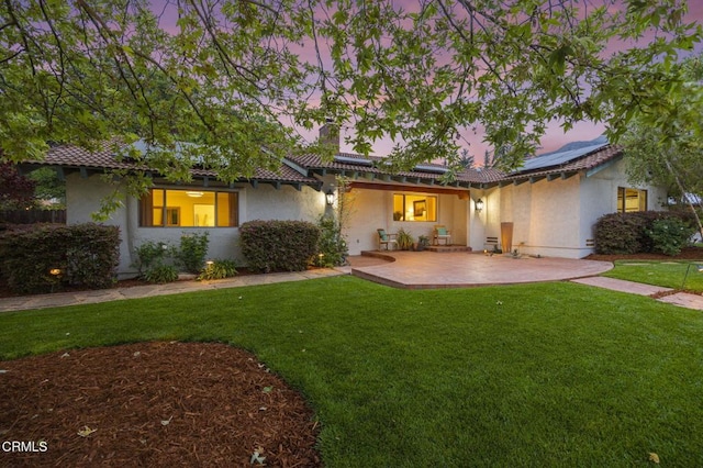 ranch-style home with a chimney, a front yard, a patio, and solar panels