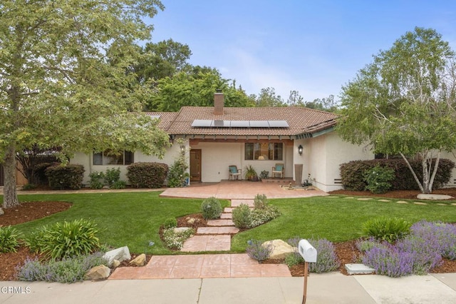 ranch-style house with a tile roof, a front lawn, roof mounted solar panels, and a chimney