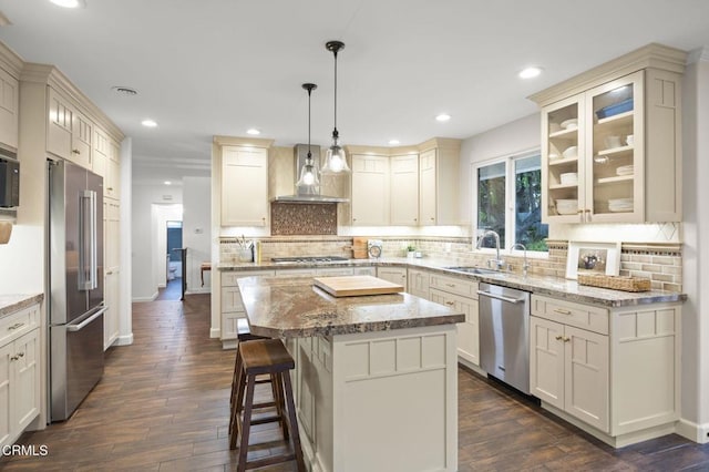 kitchen featuring a sink, a center island, wall chimney exhaust hood, appliances with stainless steel finishes, and dark wood finished floors
