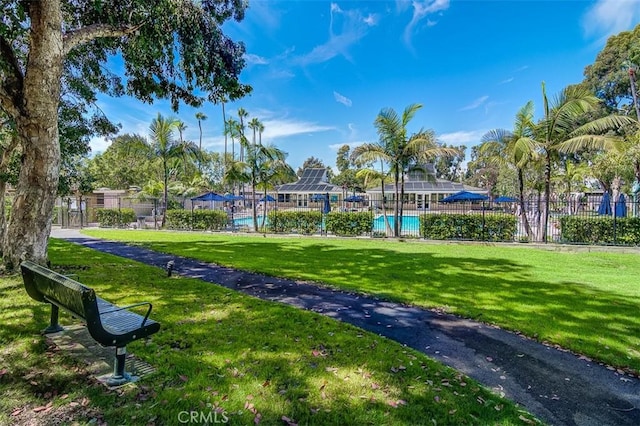 view of property's community with a pool, a lawn, and fence