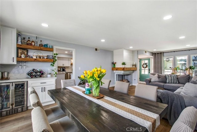 dining area featuring recessed lighting, light wood finished floors, wine cooler, a bar, and a large fireplace