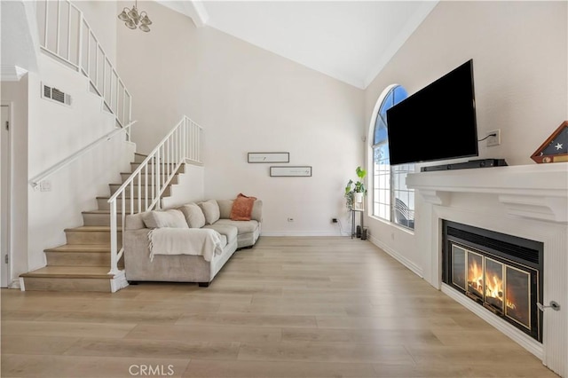 living room with stairway, high vaulted ceiling, wood finished floors, a glass covered fireplace, and visible vents