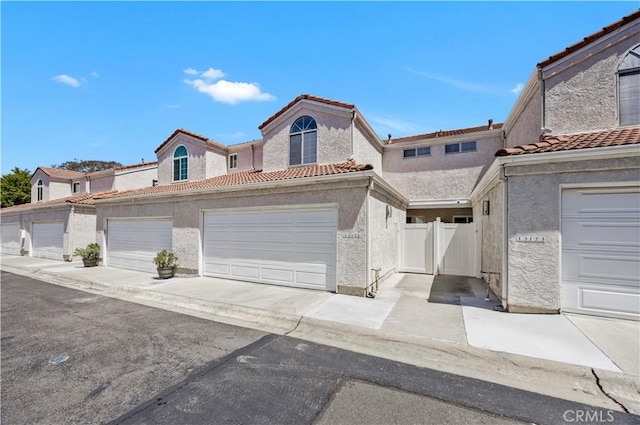 mediterranean / spanish-style house with fence, a tile roof, a garage, and stucco siding