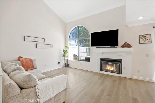 living room featuring baseboards, wood finished floors, a glass covered fireplace, and crown molding