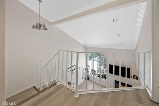 stairway with a chandelier, wood finished floors, lofted ceiling, and ornamental molding
