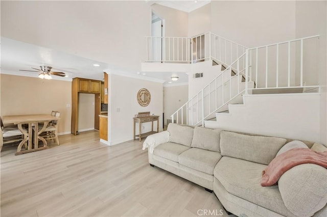 living room with ceiling fan, a towering ceiling, stairs, and ornamental molding
