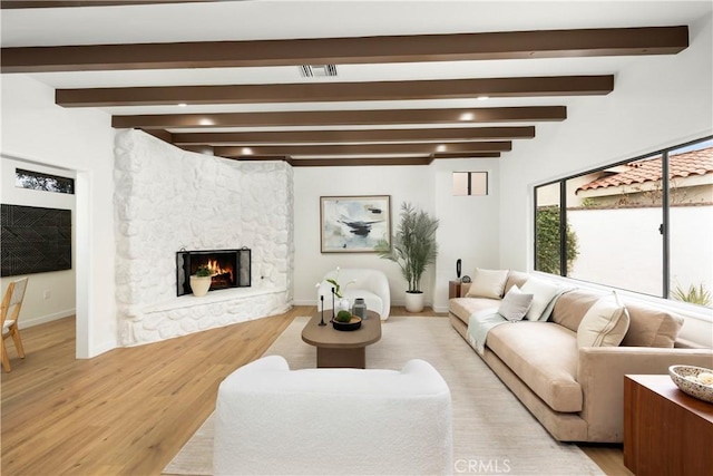 living room featuring baseboards, wood finished floors, a stone fireplace, and beamed ceiling