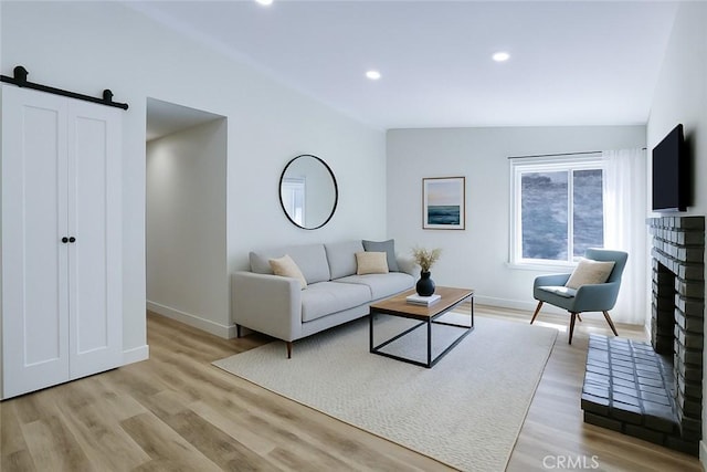 living room featuring light wood-type flooring, a brick fireplace, baseboards, and a barn door