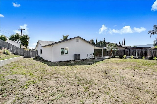 rear view of house featuring stucco siding, a fenced backyard, a yard, and central AC unit