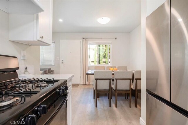809 E Acacia Ave Unit H, Glendale, CA 91205 - kitchen with black range with gas cooktop, light wood finished floors, white cabinets, wall chimney exhaust hood, and freestanding refrigerator