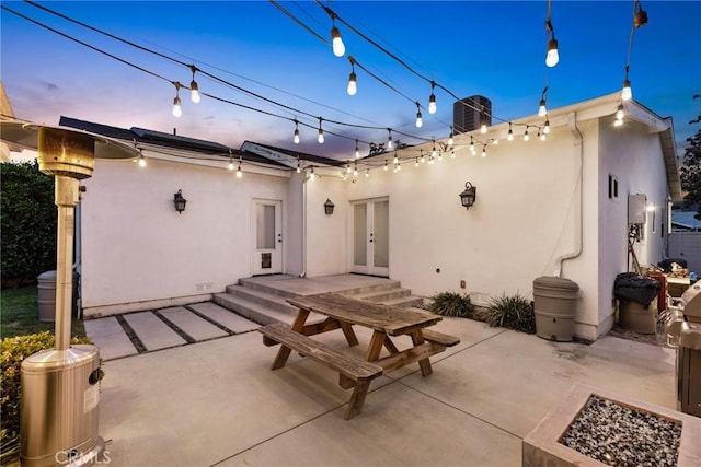 patio terrace at dusk featuring central air condition unit, a fire pit, and french doors