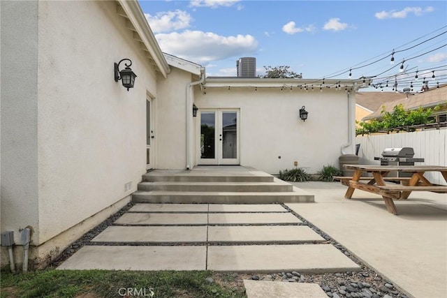 view of exterior entry with stucco siding, fence, a patio, and french doors
