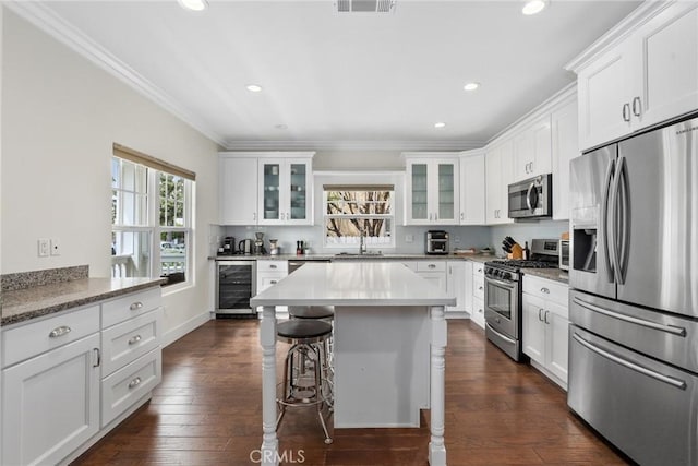 kitchen with appliances with stainless steel finishes, wine cooler, a kitchen breakfast bar, ornamental molding, and glass insert cabinets