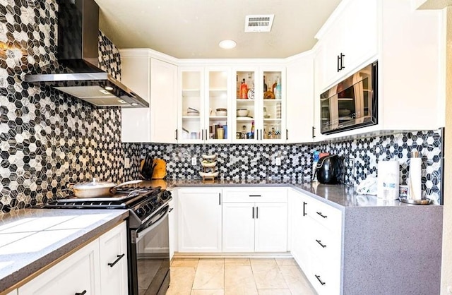 kitchen featuring light stone countertops, glass insert cabinets, wall chimney exhaust hood, black gas range, and visible vents