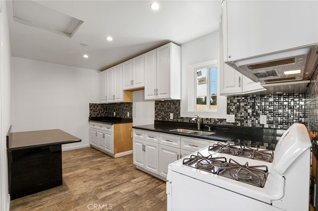 kitchen featuring white cabinets, backsplash, dark countertops, white range with gas stovetop, and a sink