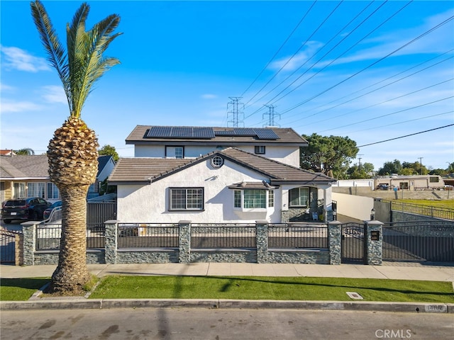 view of front of home with a gate, a tile roof, a fenced front yard, roof mounted solar panels, and stucco siding