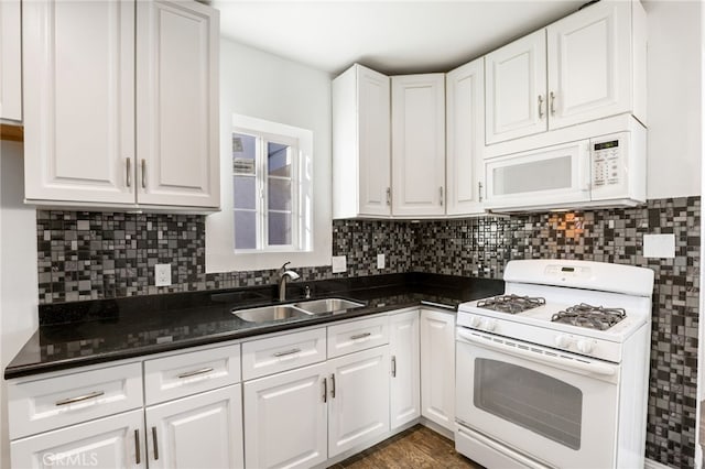 kitchen with dark countertops, white cabinetry, a sink, and white appliances