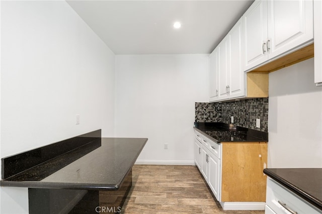 kitchen featuring white cabinets, light wood-style flooring, dark stone countertops, tasteful backsplash, and baseboards