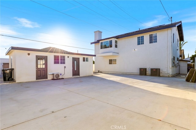 rear view of property featuring central air condition unit, a patio area, a chimney, and stucco siding