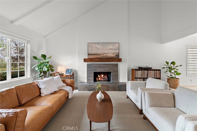 carpeted living area with beamed ceiling, a stone fireplace, and high vaulted ceiling