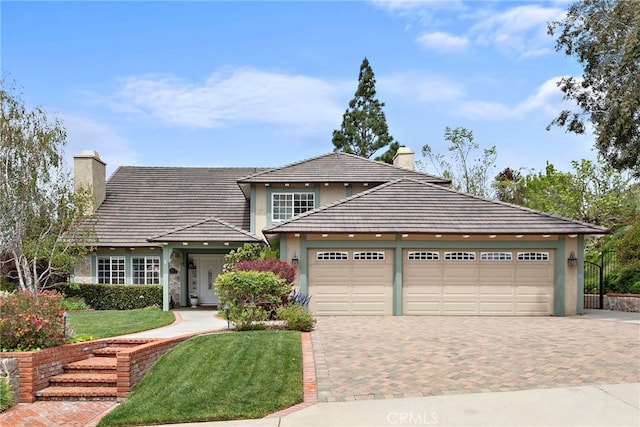 view of front of home with a front lawn, a chimney, a garage, stucco siding, and decorative driveway
