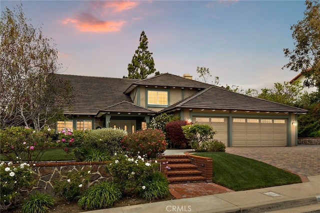 view of front of house featuring a tiled roof, driveway, a chimney, a garage, and stucco siding