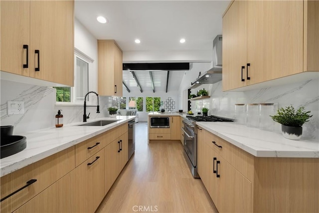 kitchen featuring wall chimney range hood, a sink, a healthy amount of sunlight, stainless steel appliances, and light brown cabinetry