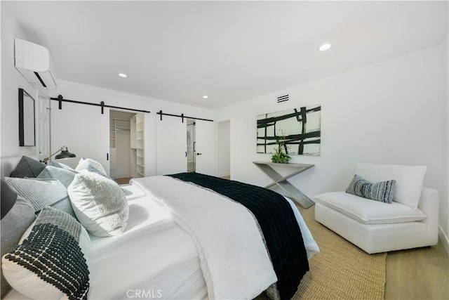 bedroom with recessed lighting, an AC wall unit, wood finished floors, and a barn door