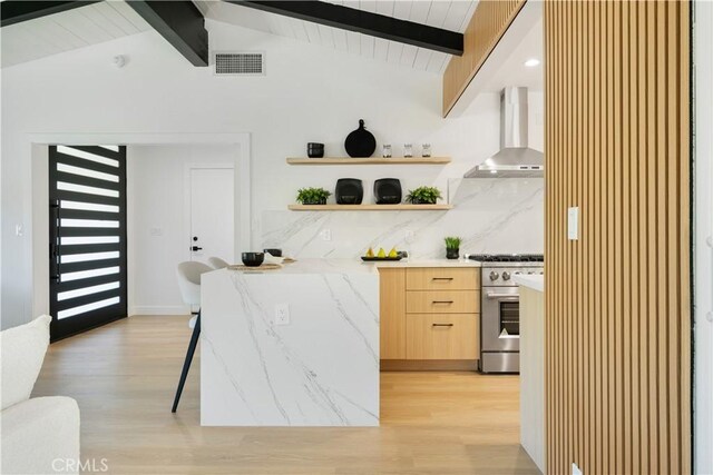 kitchen featuring high end stove, visible vents, light wood-type flooring, wall chimney exhaust hood, and modern cabinets
