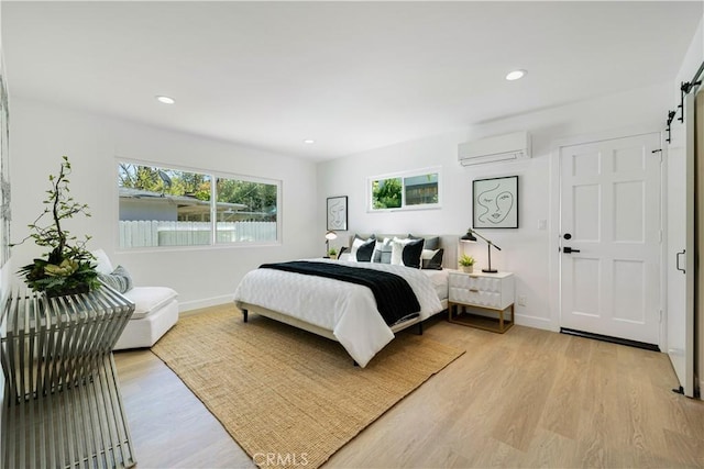bedroom with a wall unit AC, a barn door, baseboards, recessed lighting, and light wood finished floors
