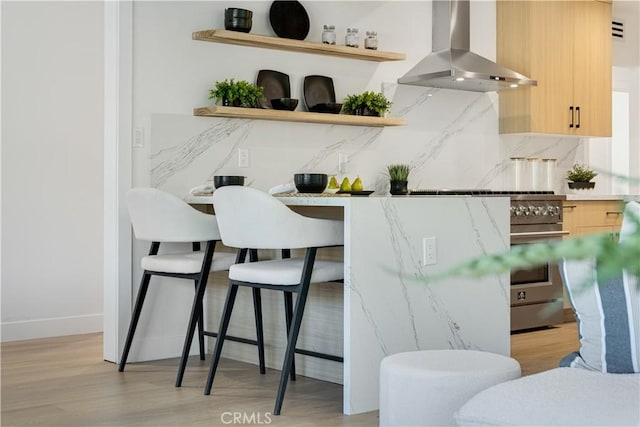 kitchen with wall chimney range hood, open shelves, baseboards, light brown cabinetry, and light wood-type flooring