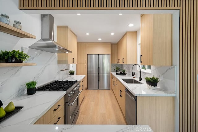 kitchen featuring wall chimney exhaust hood, light brown cabinetry, a sink, and stainless steel appliances
