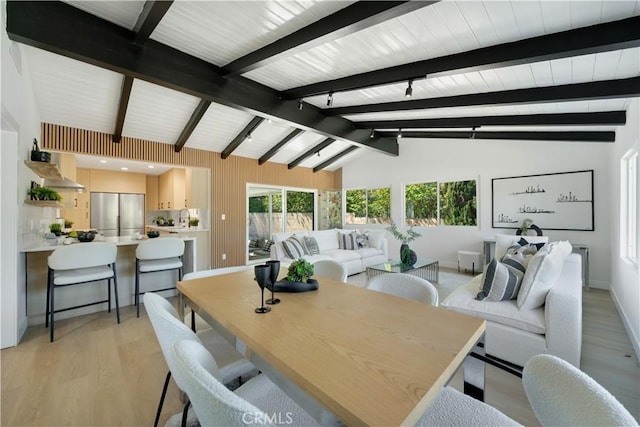 dining room featuring lofted ceiling with beams, baseboards, and light wood-type flooring