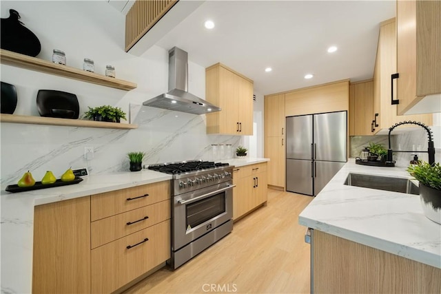 kitchen with high end appliances, light brown cabinets, open shelves, wall chimney range hood, and a sink