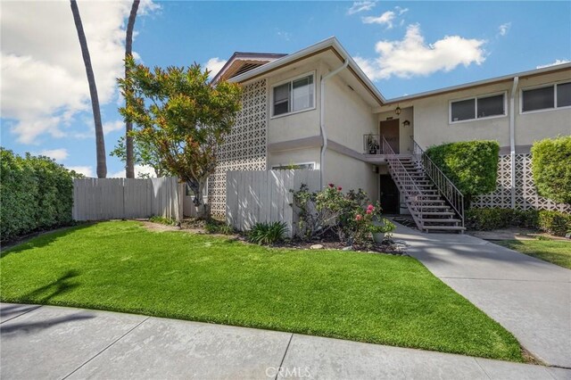 view of front of property with stairway, a front lawn, stucco siding, and fence