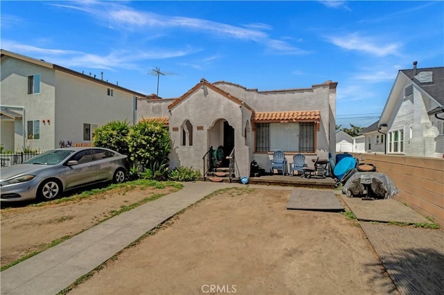 mediterranean / spanish house featuring a tiled roof, fence, and stucco siding