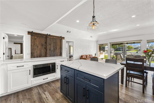 kitchen with stainless steel microwave, light stone counters, white cabinets, lofted ceiling, and dark wood finished floors