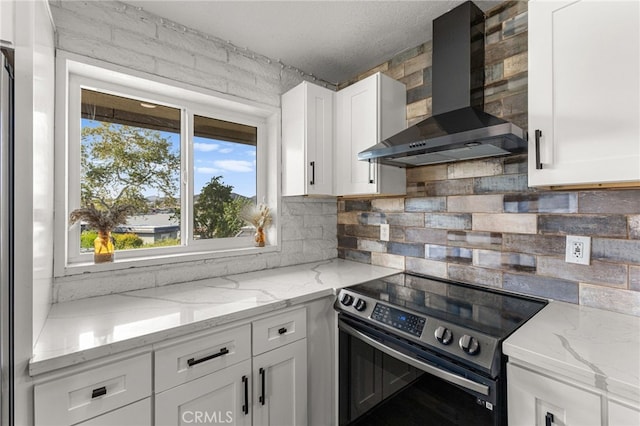 kitchen featuring wall chimney exhaust hood, white cabinets, backsplash, and electric range