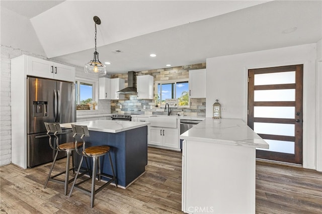 kitchen with wall chimney range hood, a sink, a breakfast bar, stainless steel appliances, and dark wood-style floors