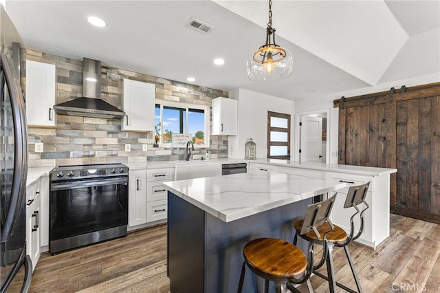 kitchen featuring stainless steel electric range, wall chimney exhaust hood, visible vents, a peninsula, and freestanding refrigerator