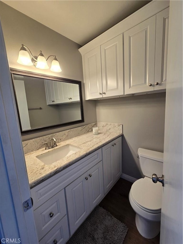 bathroom with baseboards, wood finished floors, vanity, and toilet