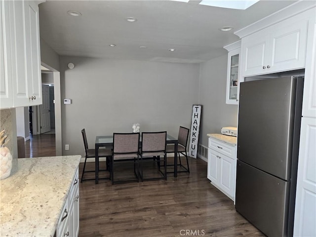 kitchen with glass insert cabinets, white cabinets, dark wood-style flooring, visible vents, and freestanding refrigerator