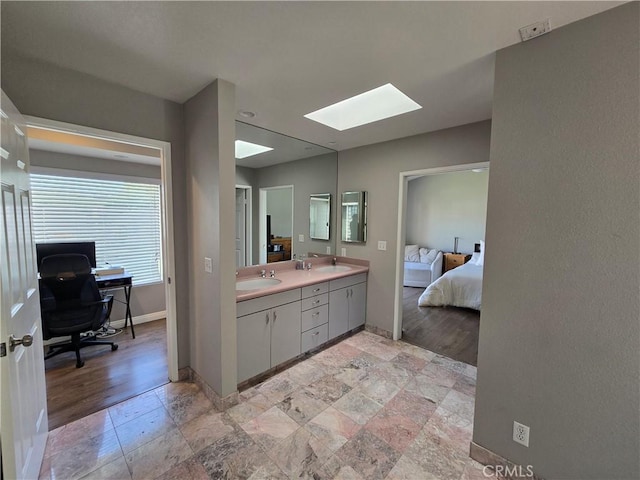 full bath with double vanity, a sink, ensuite bath, a skylight, and baseboards